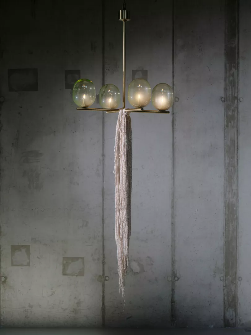 Modern chandelier with glowing orbs and rope against concrete wall.