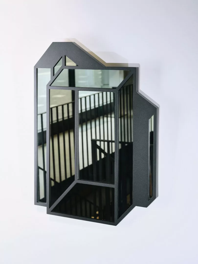 Modern house-shaped mirror on white wall.