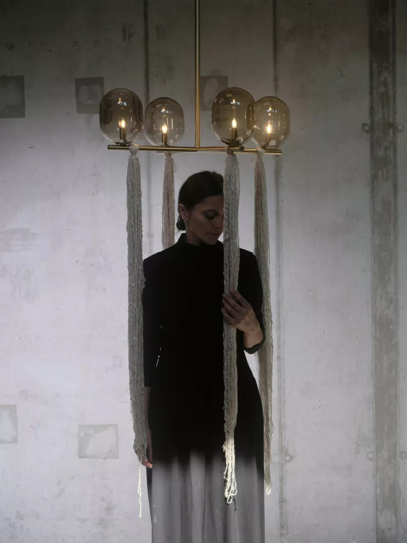 Woman observing chandelier in a dimly lit, textured room.