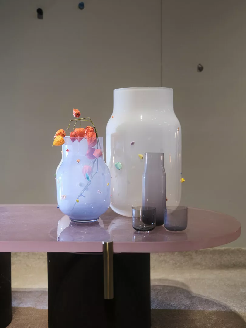 Two decorative vases with flowers on pink table.