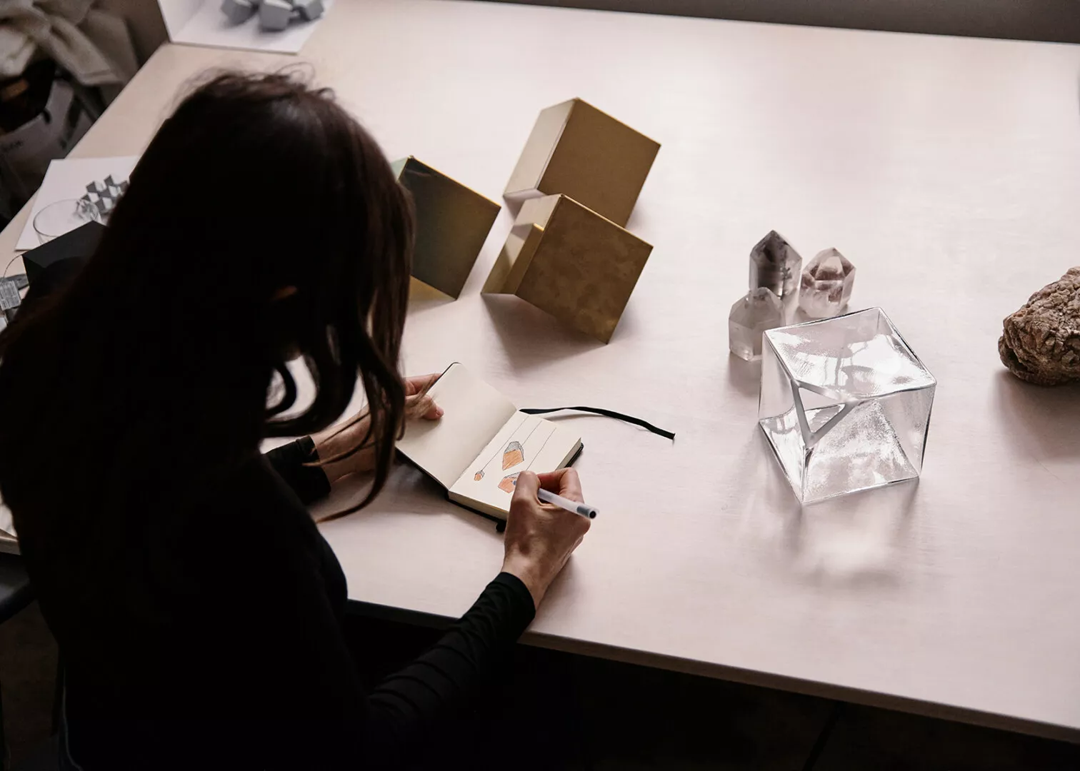 Designer sketching jewelry at desk with geometric objects.