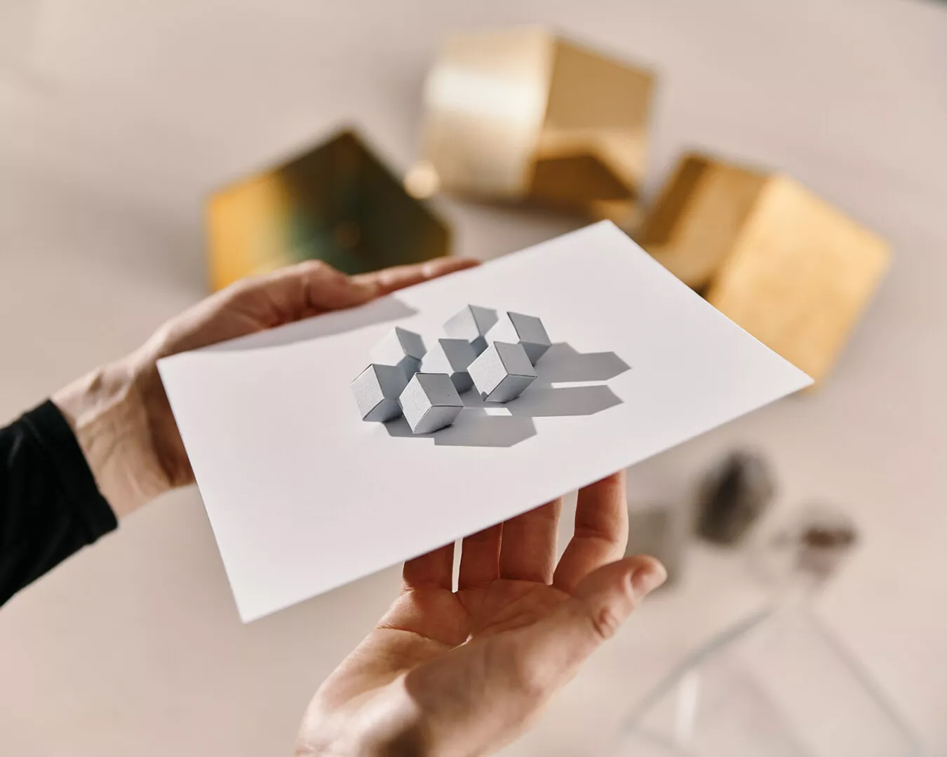 Person holding pop-up geometric card over table.