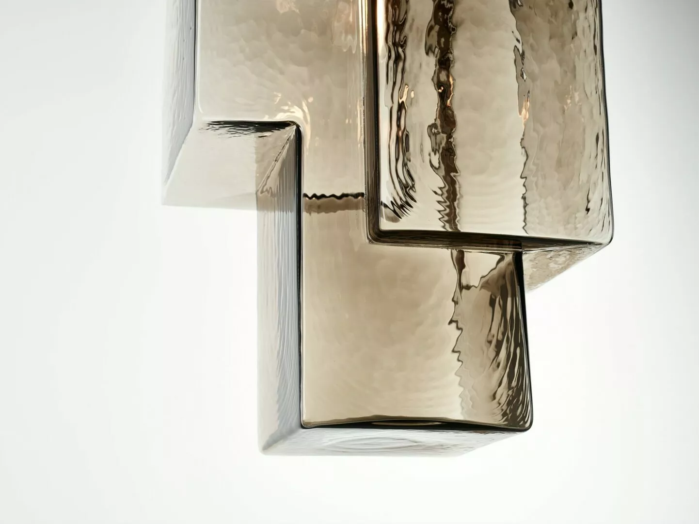 Abstract reflective glass sculpture on white background.