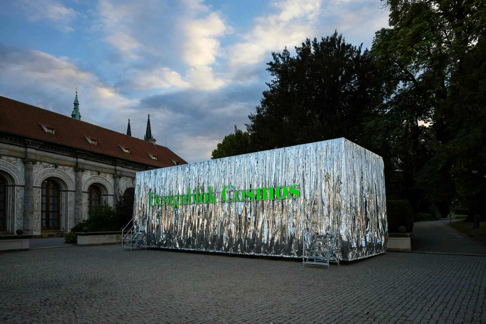 Shiny metallic art installation with 'Pszczelbok Cosmos' sign outdoors.