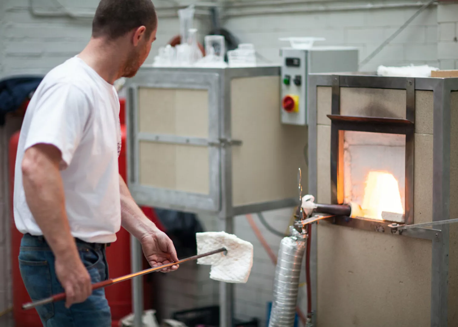 Glassblower shaping molten glass near furnace.
