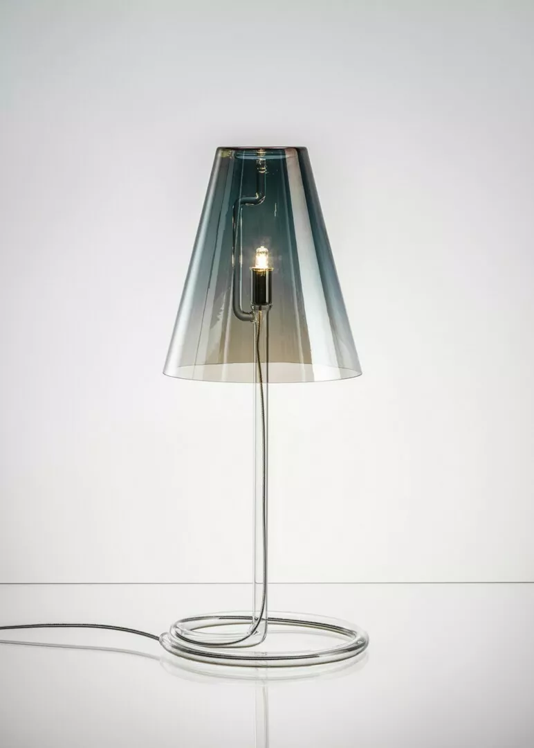 Modern clear glass table lamp lit on white background.