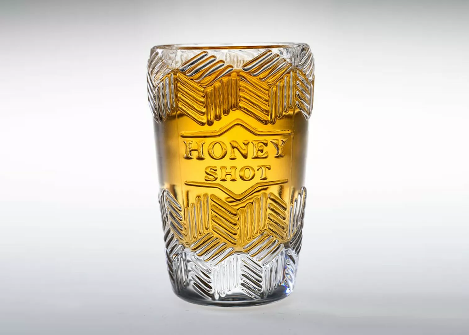 Embossed glass honey shot glass, filled.