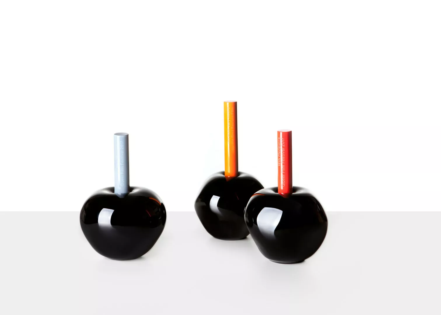 Three black vases with colorful cylindrical tops.