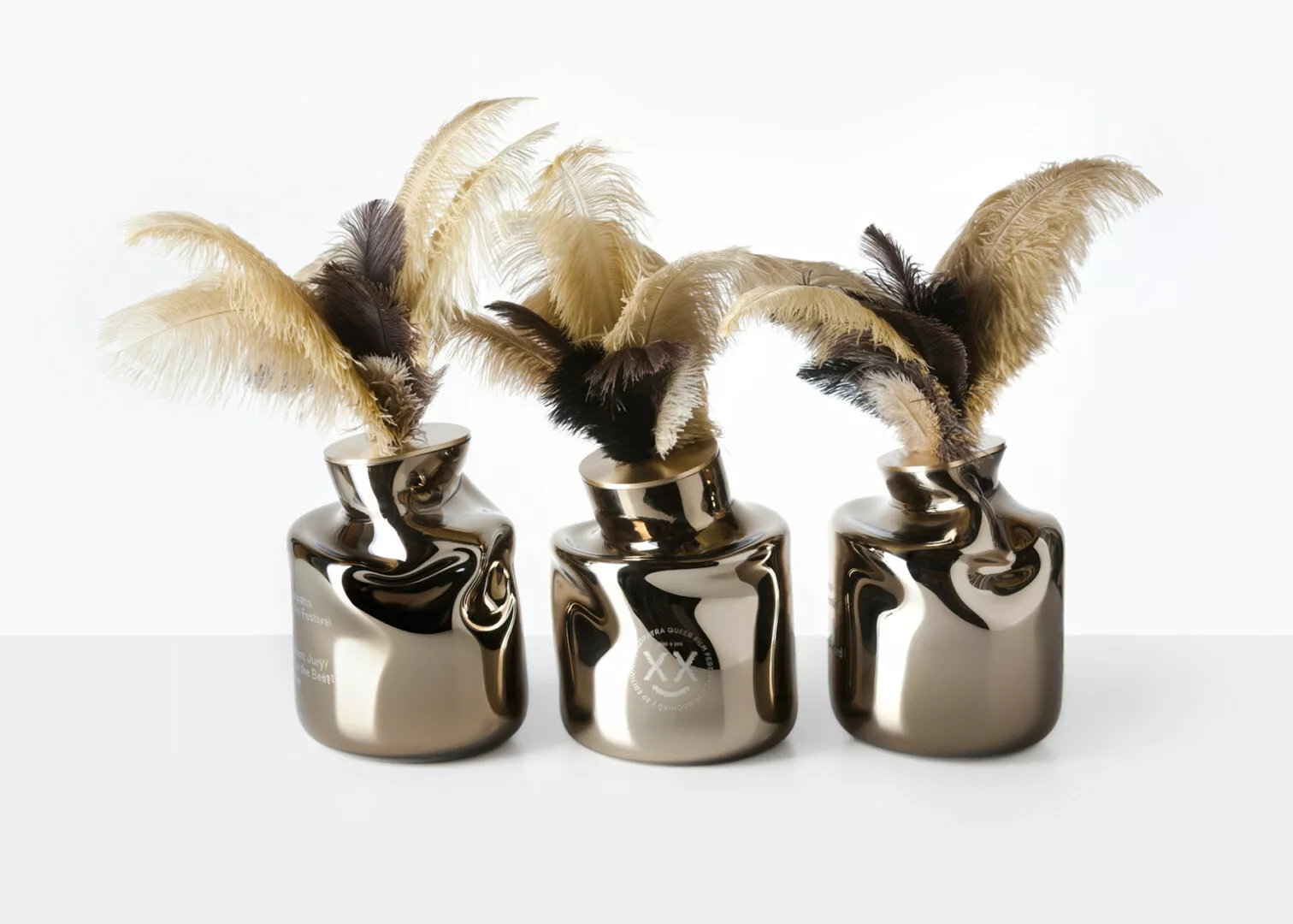 Three shiny, metallic vases with decorative feathers.