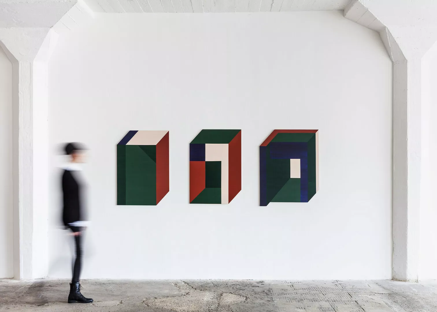 Person walking by colorful geometric sculptures in gallery.