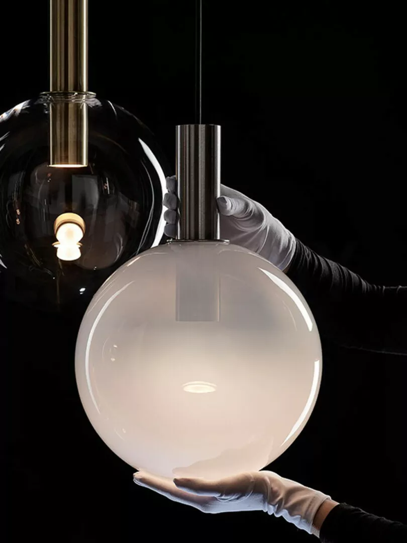 Gloved hands holding elegant glass pendant lights.