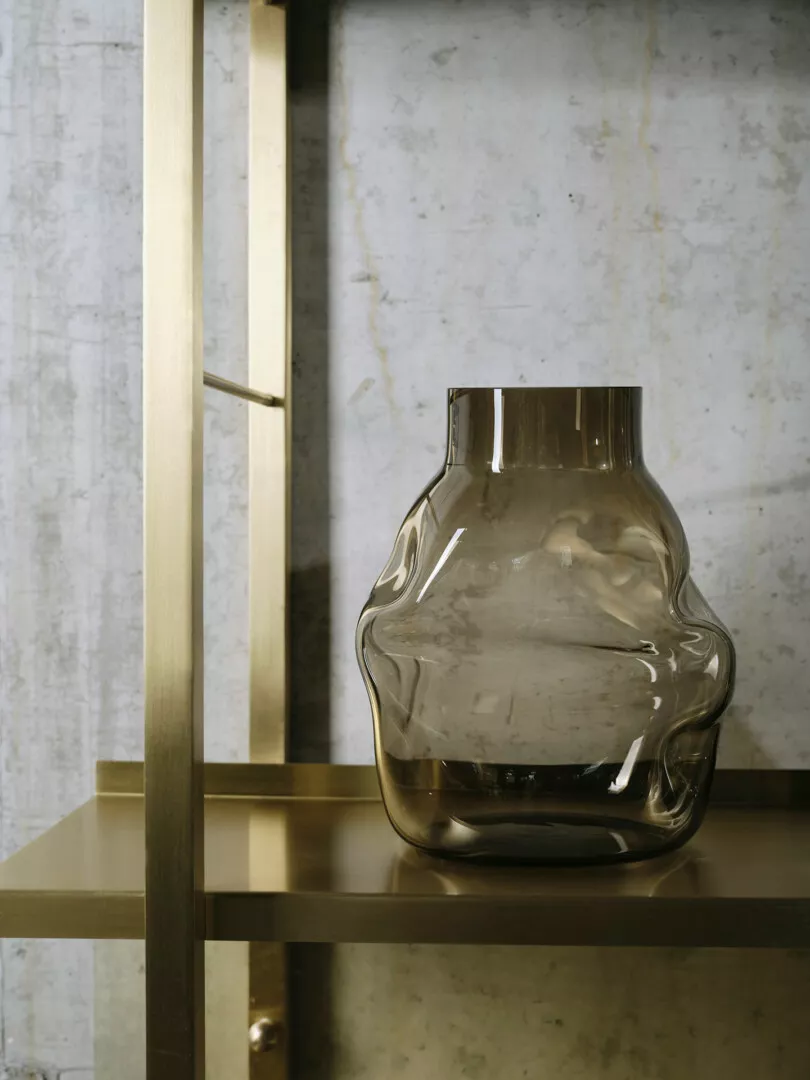 Modern glass vase on gold metallic shelf against marble.