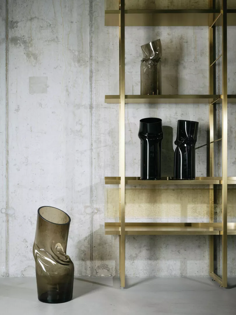 Modern glass vases on elegant gold shelves against concrete wall.
