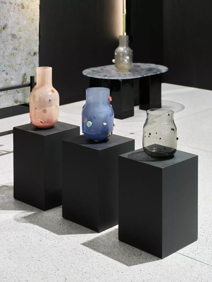 Colorful glass vases on black display pedestals, modern art.
