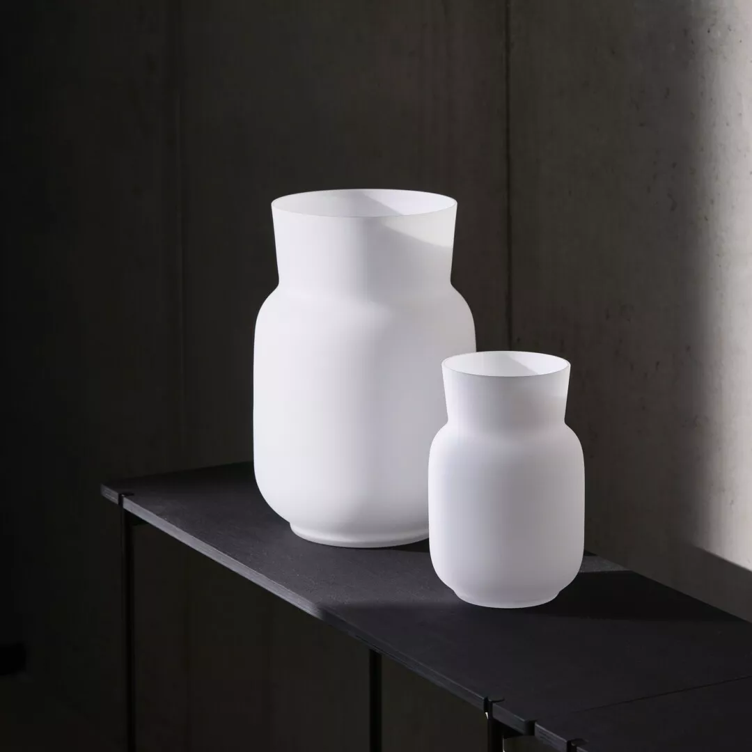 Two white ceramic vases on dark shelf, modern design.