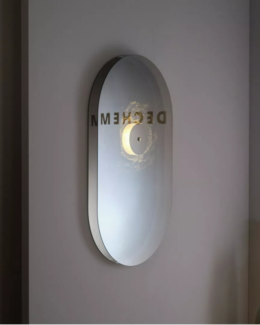 Modern oval wall sconce with "DEFENSE" text reflection.
