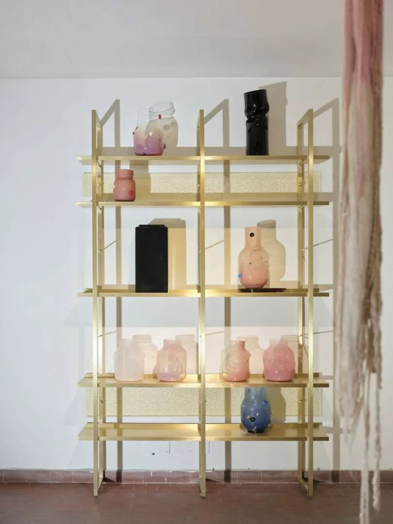Brass bookshelf with assorted colorful ceramic vases.
